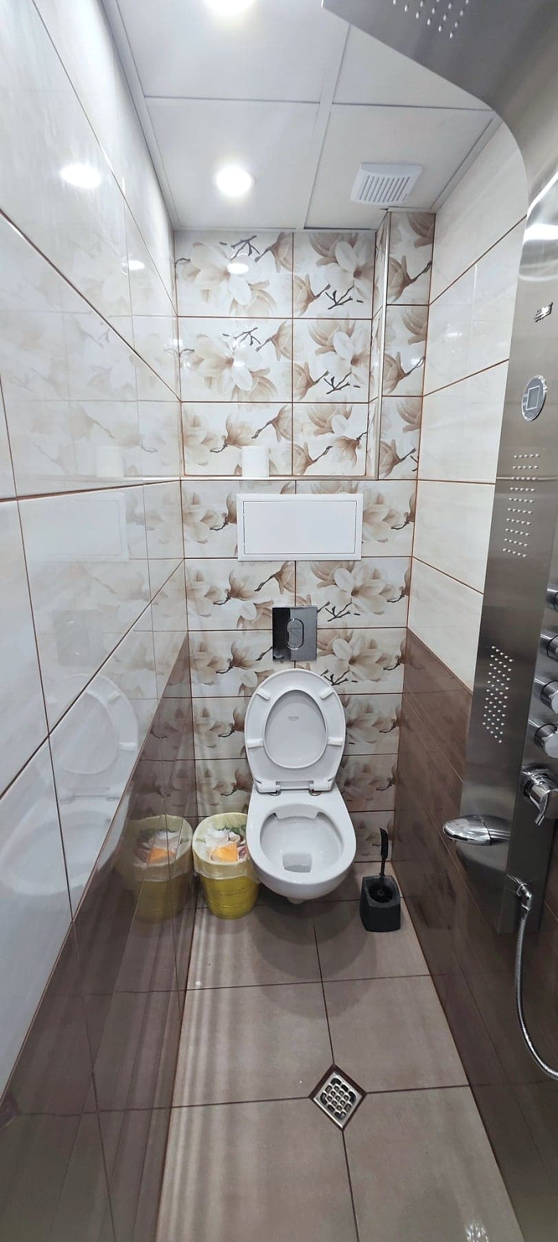 Bathroom with floral tiles and a shower panel — Wall-hung toilet