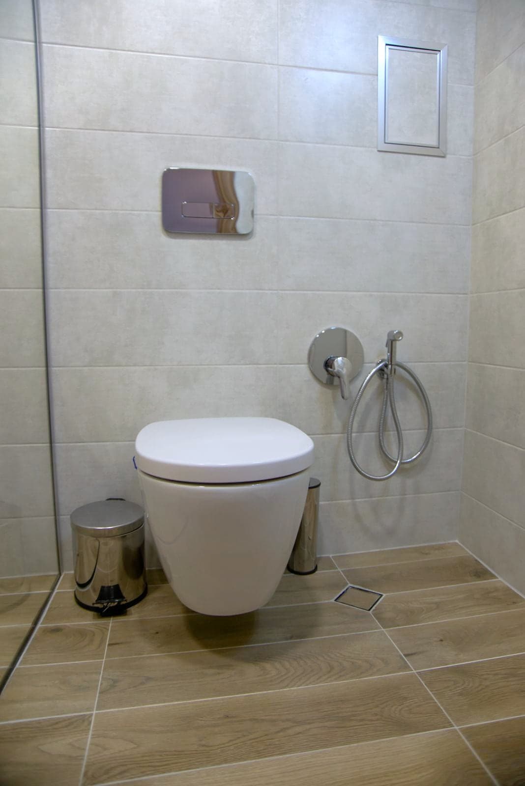 Bathroom with a glass shower and a wood-effect floor — Wall-hung toilet with a bidet shower