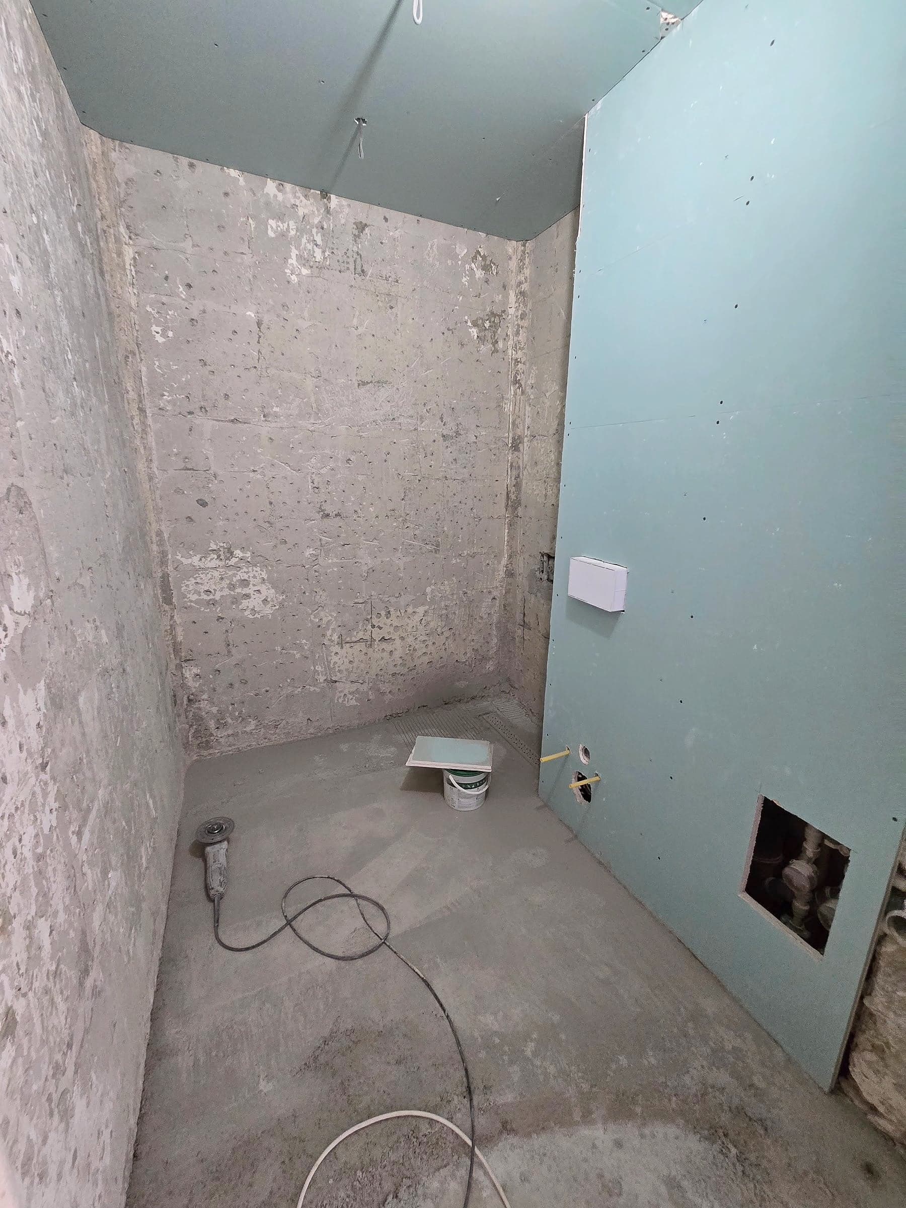 The same bathroom with a new screed, a suspended ceiling and a wall lined with moisture-resistant plasterboard, with an opening onto the pipes and the water meters