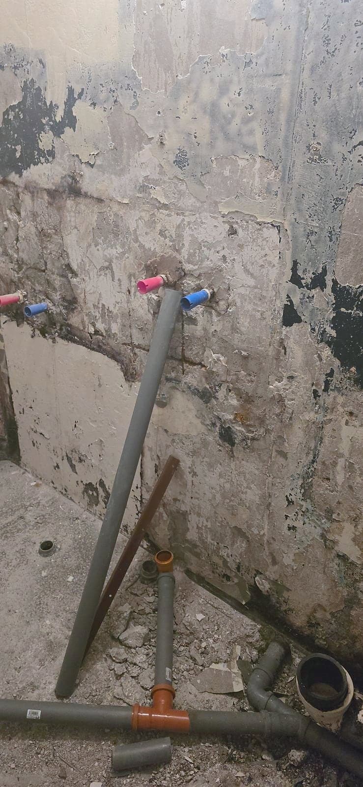 Стена в баня със следи от свалените плочки, нови изводи за топла и студена вода и канализационни тръби на пода
