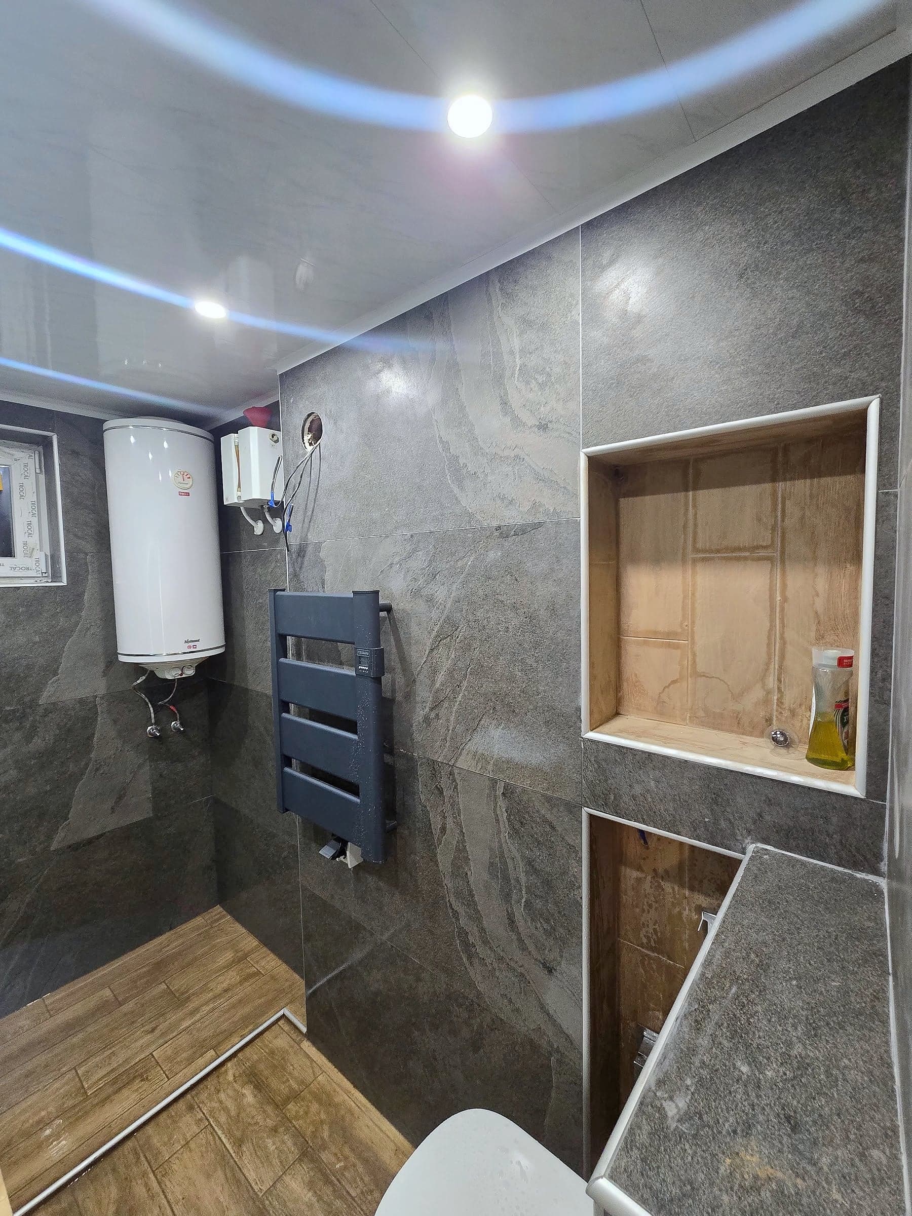 Bathroom in Bankya: grey stone and a wood-effect floor — Niches lined with wood-effect tiles, radiator and water heater
