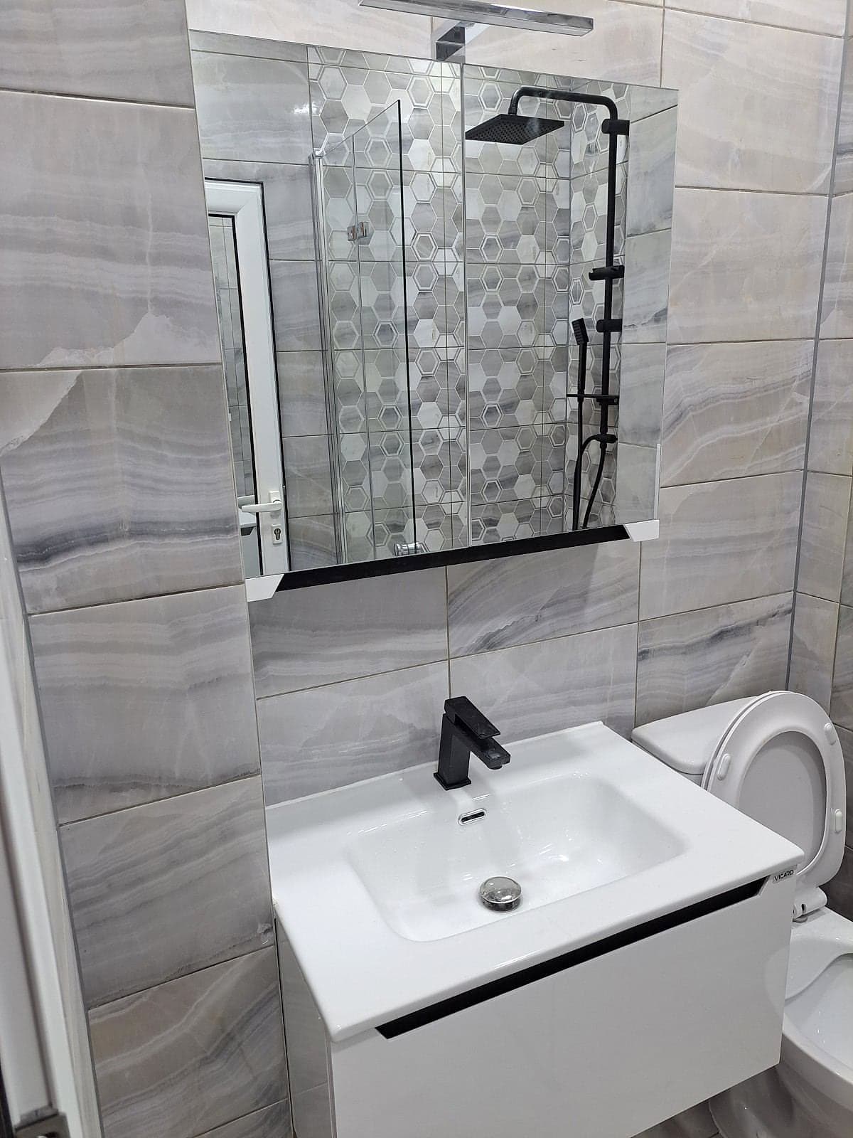 Grey bathroom with hexagon tiles and black taps — Vanity unit and mirror