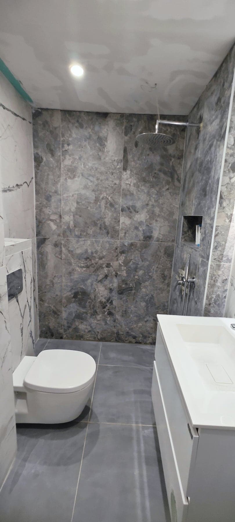 Dark stone and white marble bathroom with an LED mirror — Dark stone shower area and wall-hung toilet