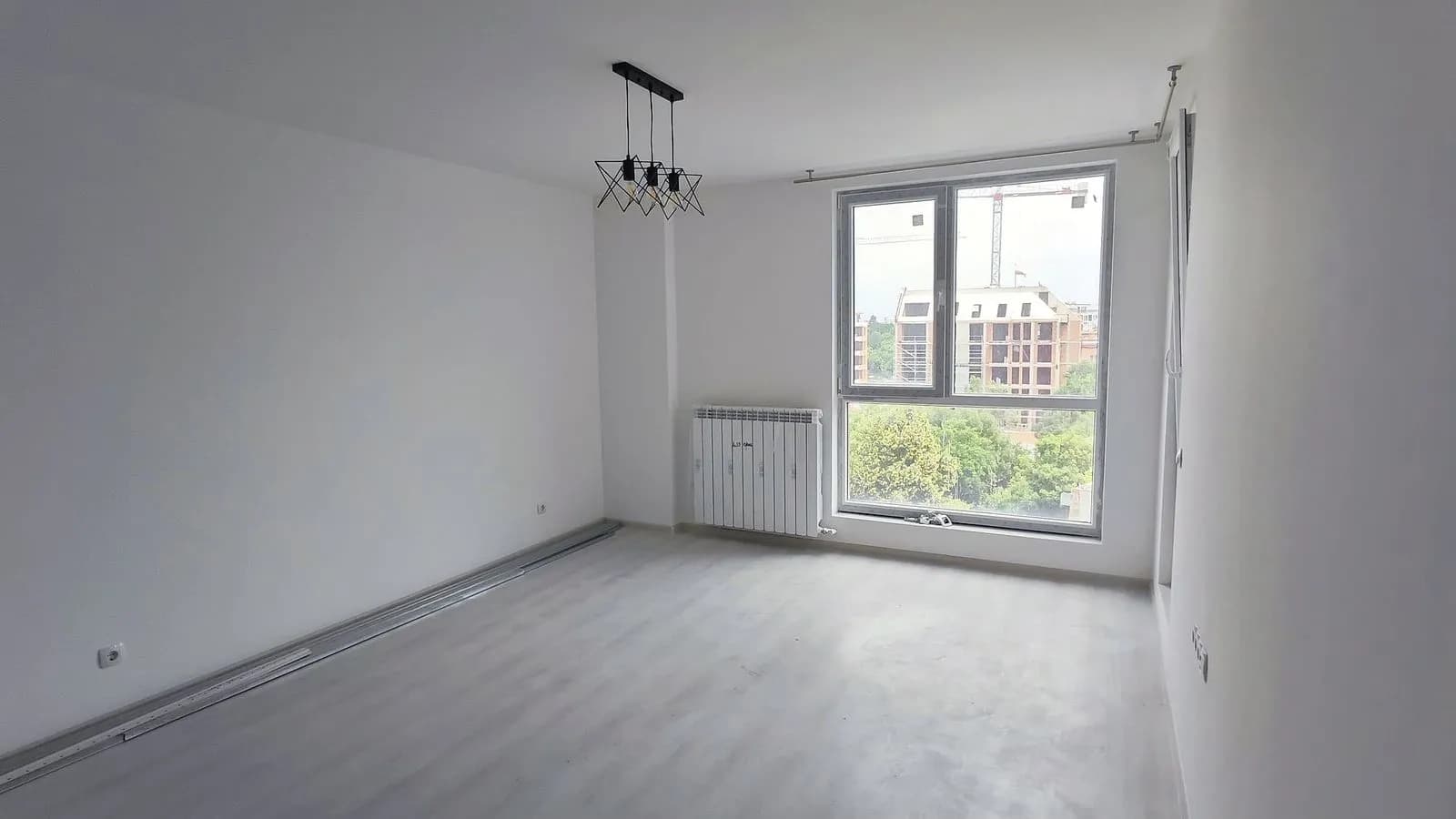 A living room in an apartment in Ovcha Kupel after the renovation: white walls, light laminate flooring and a pendant light