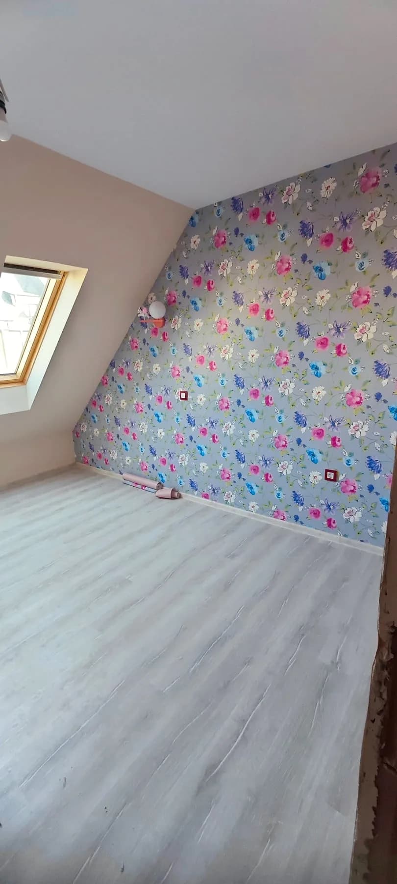 Attic room: a wall with floral wallpaper, a sloping ceiling with a roof window and grey laminate flooring
