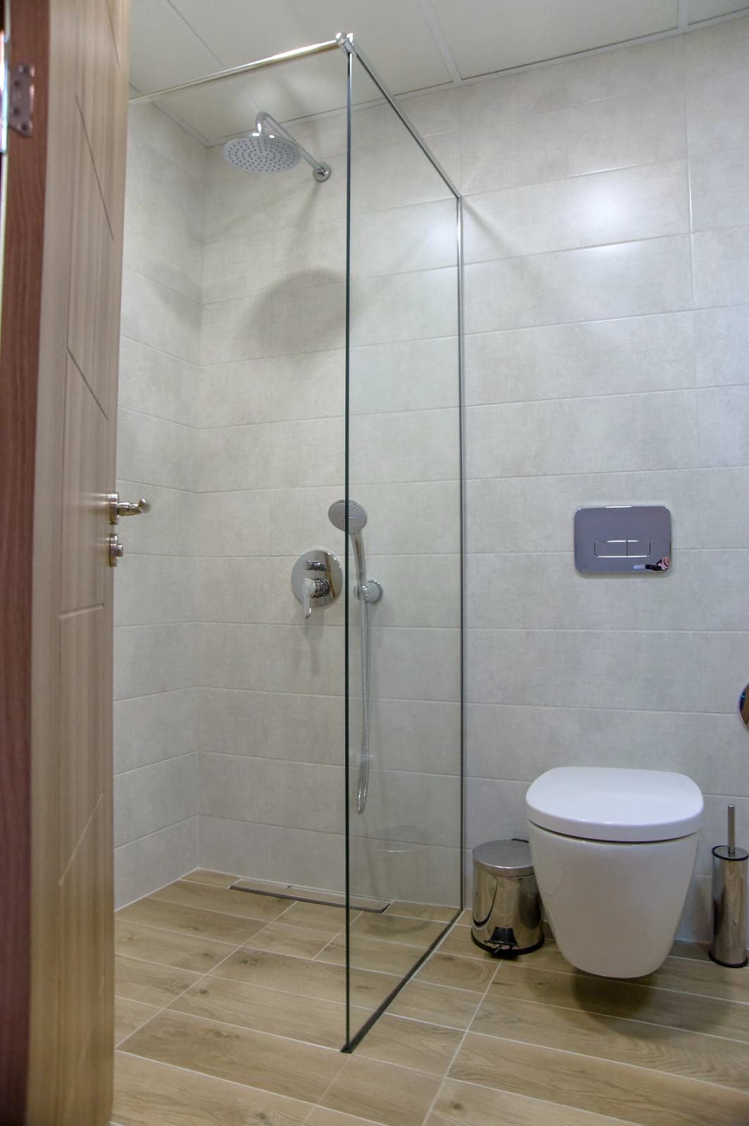 Bathroom with a glass shower and a wood-effect floor — Shower area with a glass panel and wall-hung toilet