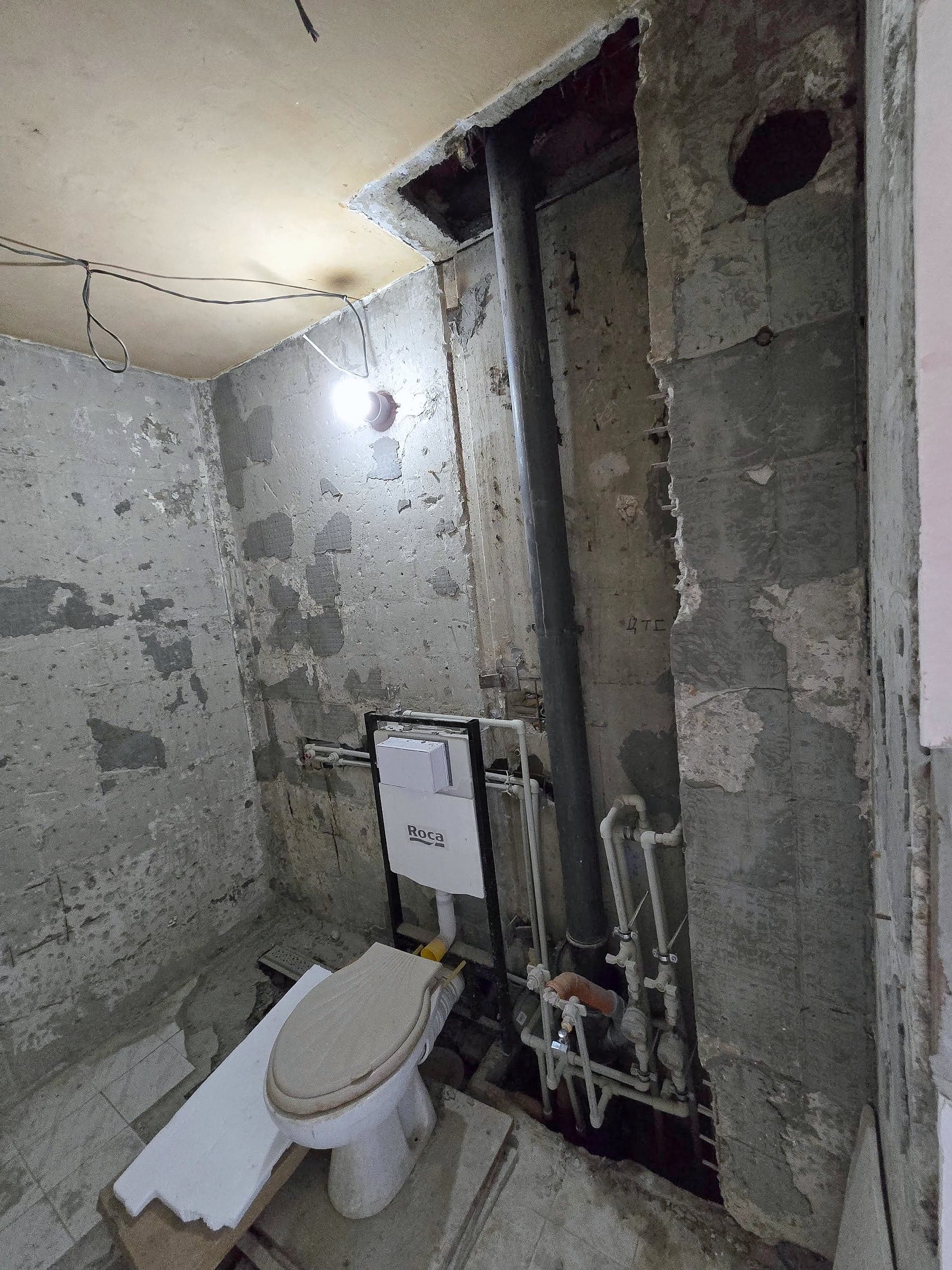 Exposed riser in the corner of the bathroom, new pipes with valves and water meters next to it, and a concealed frame for a wall-hung toilet